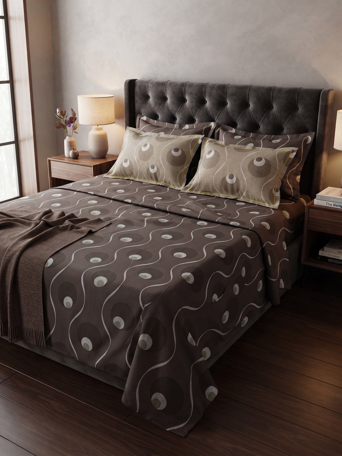 A bed dressed in a dark brown and beige patterned bedding set, featuring a tufted dark gray headboard, wooden nightstands, and warm bedside lighting in a styled bedroom setting.