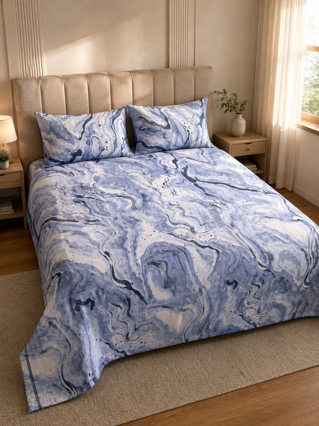 A bed dressed in a blue and white marble-patterned duvet cover and matching pillowcases, styled in a warm, modern bedroom with beige walls, wooden nightstands, and a window with sheer curtains.