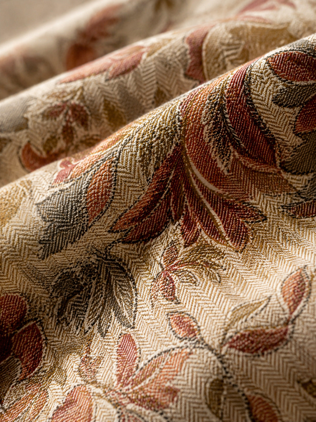 A close-up of draped fabric with a woven floral pattern in muted rust red, taupe, olive, and cream tones.
