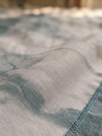 Close-up of a lightweight woven fabric with a mottled blue and gray pattern and a visible stitched edge.