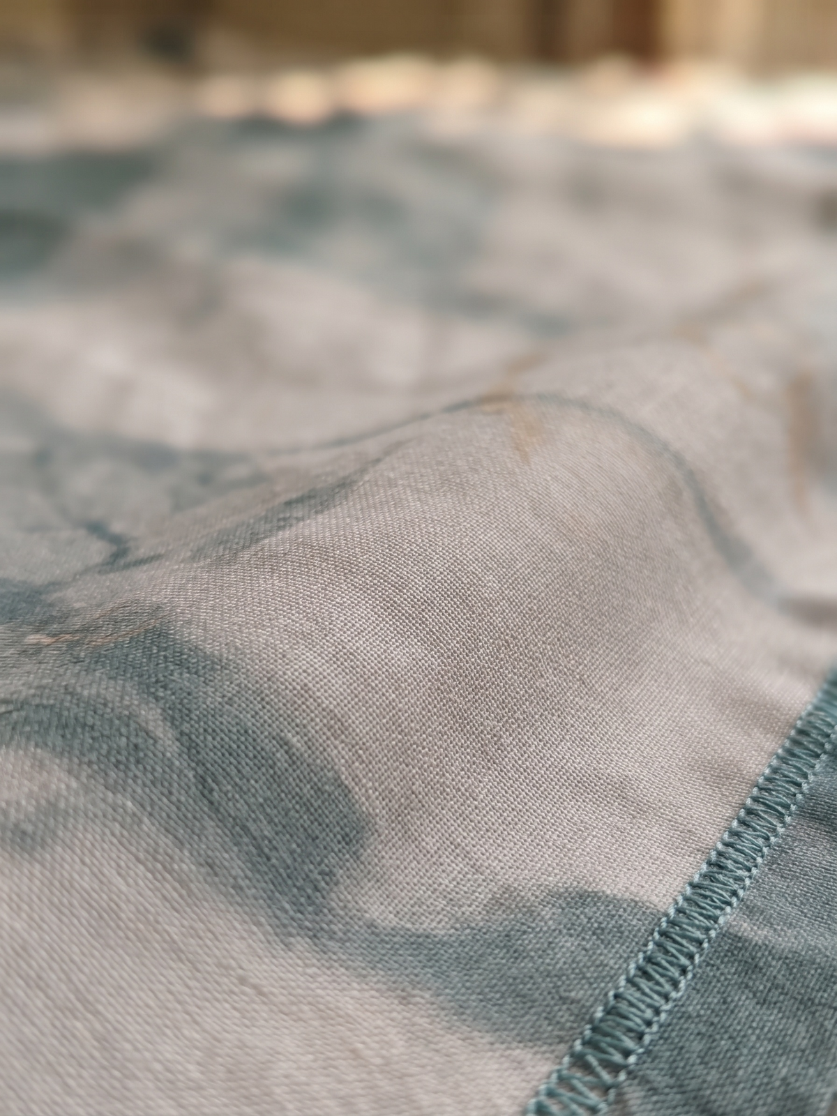 Close-up of a lightweight woven fabric with a mottled blue and gray pattern and a visible stitched edge.