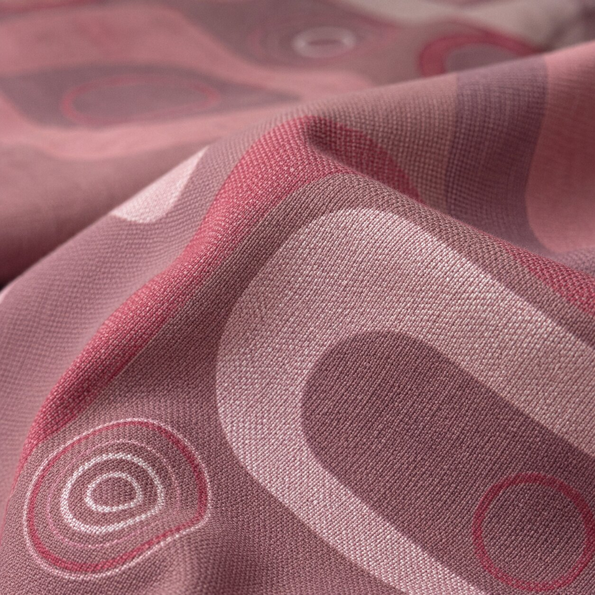 A close-up of draped fabric with an abstract geometric pattern in dusty pink, mauve, and light blush tones.