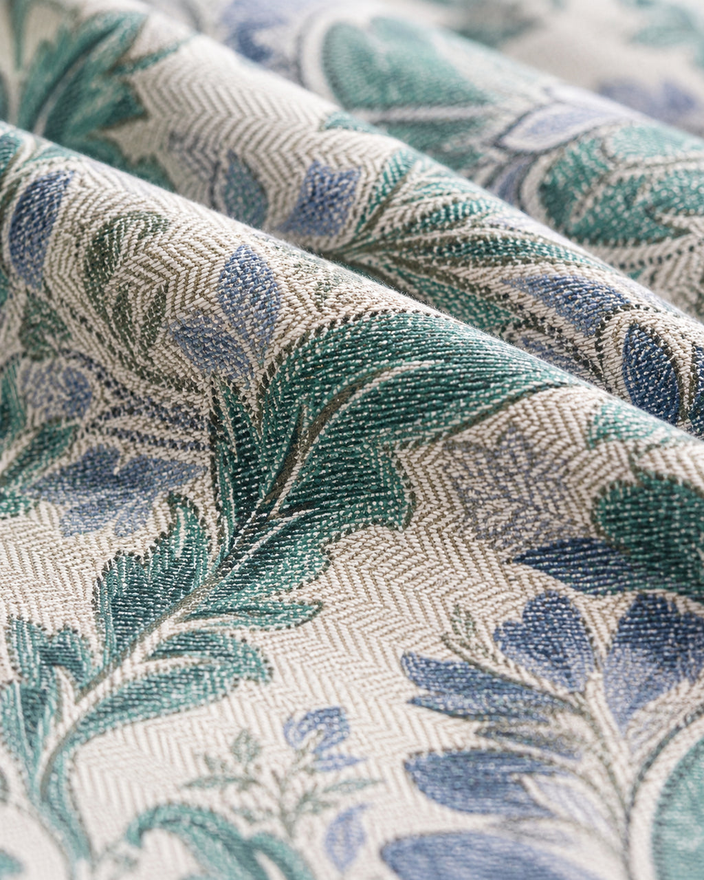 A close-up of draped fabric with a woven botanical pattern in teal green, dusty blue, and cream.