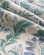 A close-up of draped fabric with a woven botanical pattern in teal green, dusty blue, and cream.