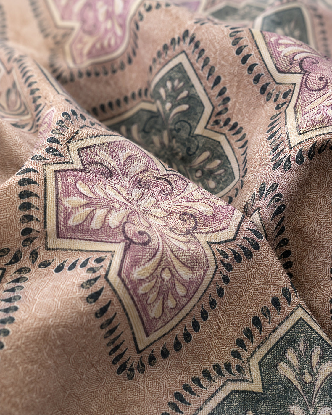 A close-up of patterned fabric with a beige base and ornate medallion motifs in dusty pink, dark green, and cream.