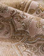 A close-up of draped fabric with an ornate paisley and scroll pattern in warm beige, tan, and brown tones on a light cream background.