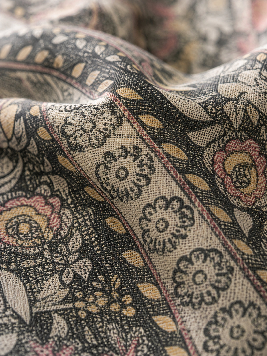 A close-up of a draped fabric with a detailed botanical pattern in black, beige, muted gold, and dusty pink.