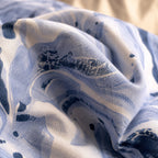 A close-up of a lightweight fabric with an abstract watercolor-style print in shades of blue, navy, and off-white, shown in soft folds.