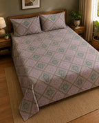 A bed dressed in a patterned quilt and matching pillow shams, shown in a styled bedroom with wooden furniture, plants, and a window.