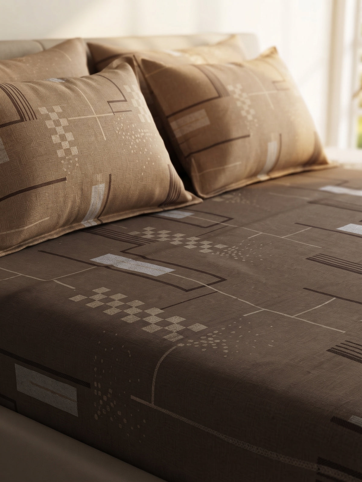 A bed dressed in a brown geometric-patterned sheet and matching pillowcases, photographed in a softly lit bedroom setting.