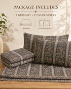 A bedding set displayed on a wooden surface against a warm beige wall, with text at the top stating 'PACKAGE INCLUDES 1 BEDSHEET + 2 PILLOW COVERS' and simple line drawings indicating the included items. The bedding has an ornate floral and paisley pattern in muted gray, beige, and dusty pink tones.