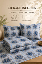 A bedding set displayed on a bed with two matching pillowcases and a folded bedsheet, featuring a blue and white floral geometric pattern. Text at the top reads 'PACKAGE INCLUDES 1 BEDSHEET + 2 PILLOW COVERS' with simple line icons, set against a warm beige wall with decorative shadows and a vase of greenery.