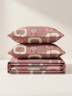 A folded bedding set with two matching pillowcases stacked on top of each other, featuring a retro mid-century modern geometric pattern in dusty red, beige, and gray on a warm cream background.