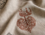 A close-up of a textured beige fabric with a reddish-brown printed motif of a stylized tree and decorative elements.