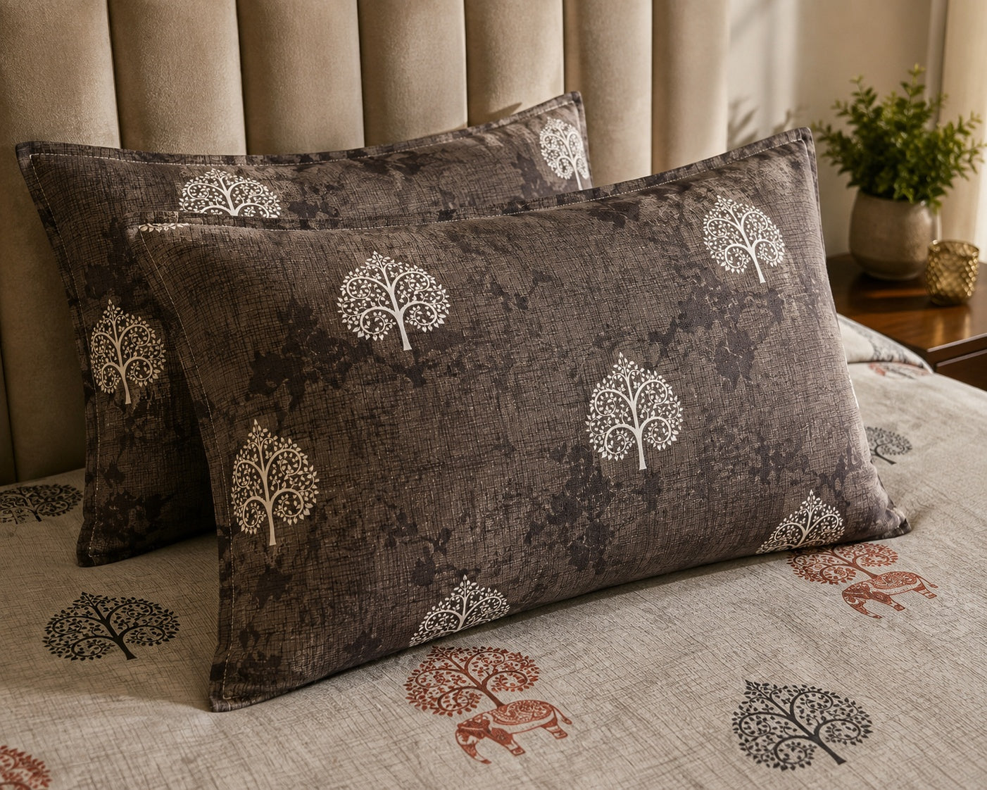 Two rectangular throw pillows with a dark brown textured fabric and a white tree pattern, styled on a bed with a matching beige duvet and a beige tufted headboard.