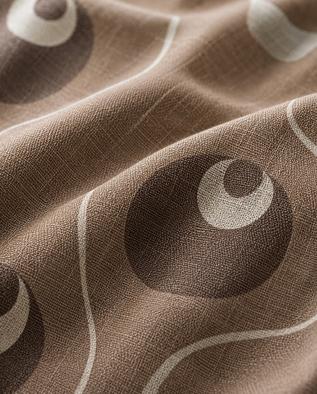 A close-up of a brown woven fabric with a repeating pattern of dark brown circles and light cream curved lines.