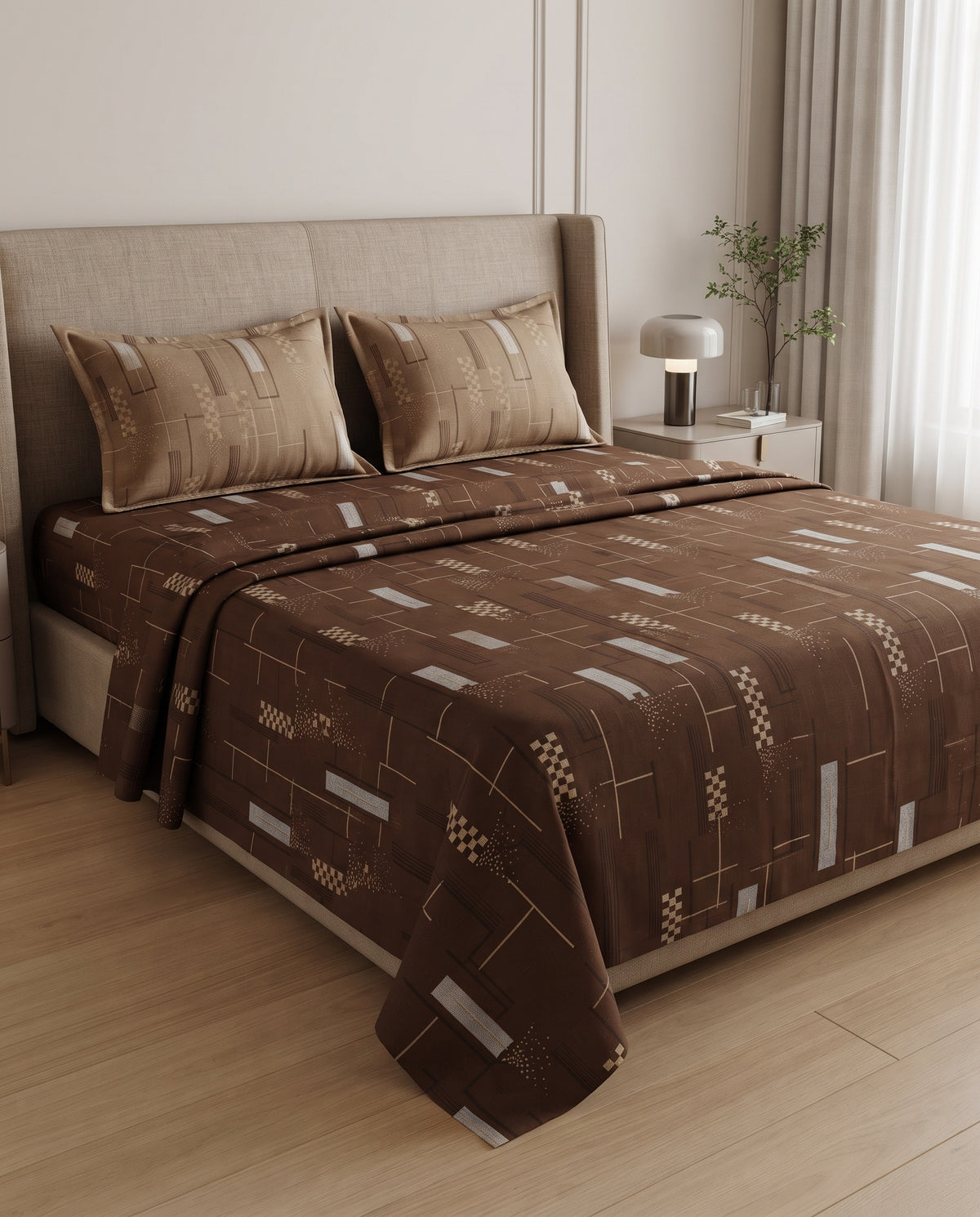 A bed dressed in a brown patterned quilt and matching pillow shams, styled in a modern bedroom with a beige upholstered headboard, bedside lamp, and light wood flooring.