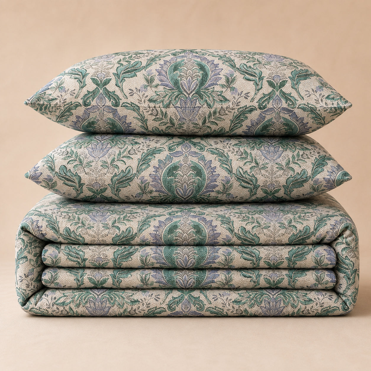 A stack of three matching upholstered home textiles with an ornate damask-style floral pattern in muted green and lavender on a warm beige background, photographed against a plain beige backdrop.