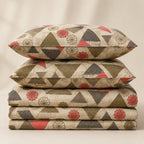 A stack of four decorative pillows with a geometric and floral pattern in olive green, charcoal gray, red, and cream, set against a warm beige background.
