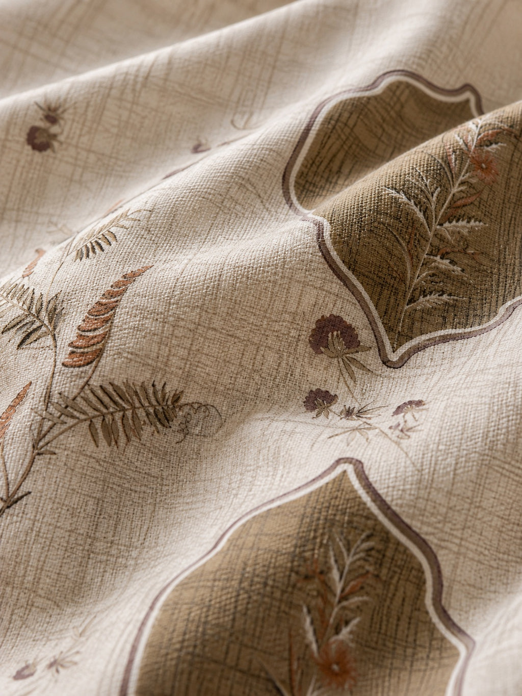 A close-up of draped beige fabric with a subtle woven texture and embroidered botanical motifs in brown, taupe, and muted rust tones.