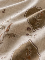 A close-up of draped beige fabric with a subtle woven texture and embroidered botanical motifs in brown, taupe, and muted rust tones.