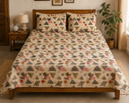 A bed dressed in a cream-colored geometric print bedding set with matching pillowcases, styled in a warm, rustic bedroom setting with a wooden headboard, bedside table, lamp, and potted plant.